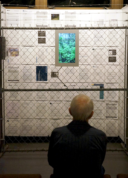 man looking at video signnage hanging on chain link fence with super fund documents behind